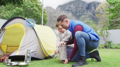 Happy-caucasian-father-with-son-preparing-camp-with-tent-in-garden