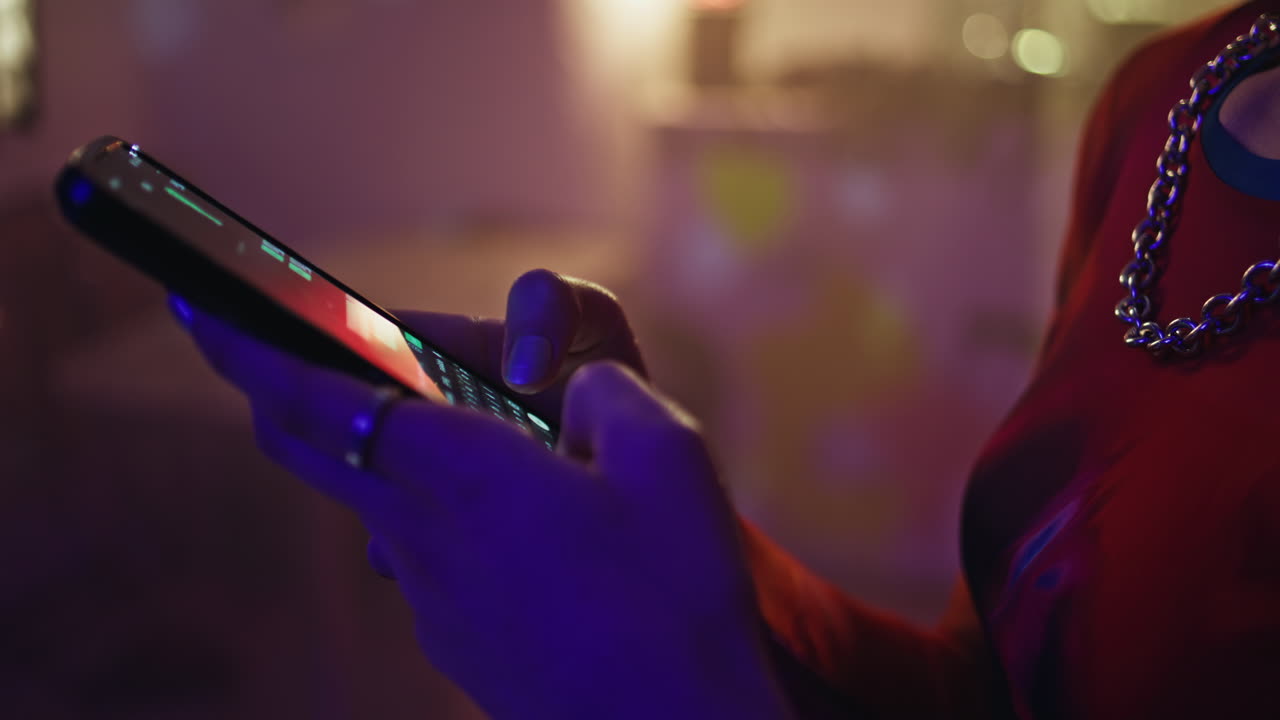 Woman hands texting smartphone in neon club glow closeup. Party girl messaging