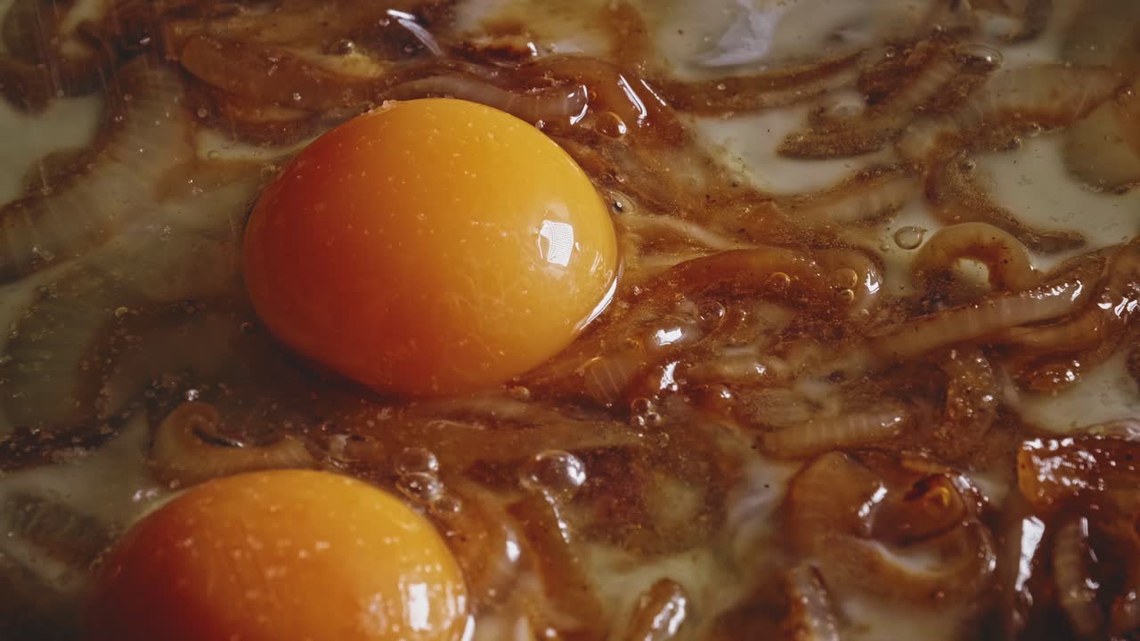 Macro shot of egg yolks floating on their whites mixed with fried onion, adding salt to it