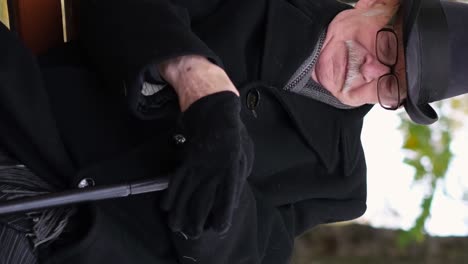 an elderly man in black clothes sits on a park bench and puts on black gloves an elderly man in black clothes sits on a park bench and puts on black gloves rest in the autumn park
