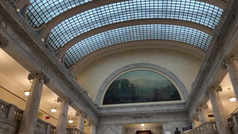 panning up and across the glass ceiling of the utah state capital to reveal hand painted murals and chandelier then down to see beautiful marble walls, pillars, and stairs