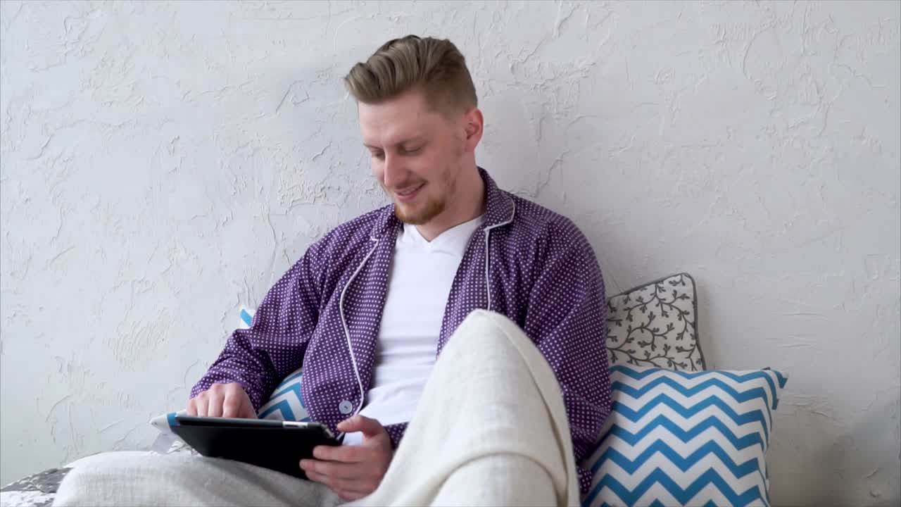 Homem vestido usando um tablet na cama