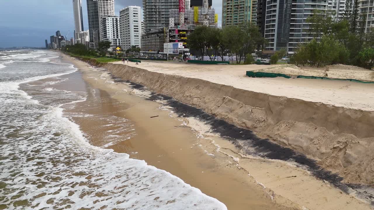 Aerial view of ocean waves eroding sandy cliffs along Gold Coast, Australia, highlighting environmental impact and urban proximity