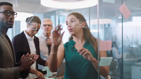 business-team-meeting-using-sticky-notes-brainstorming-colleagues-working-on-problem-solving-strategy-writing-on-glass-whiteboard-thinking-of-solution-for-project-in-office