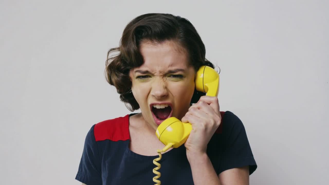 Reacting woman navy top red patches holding yellow handset shouting during shocking call at studio