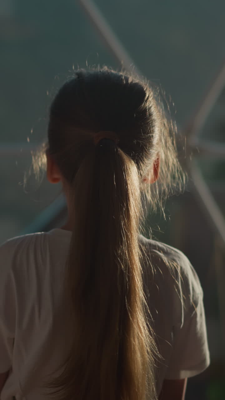 아이는 글램핑에서 유리  아래에서 걸어다니며, 작은 소녀는 호텔에서 금속 프레임으로 투명한 벽을 관찰합니다. 아이는 창문에서 반사되는 것을 봅니다.