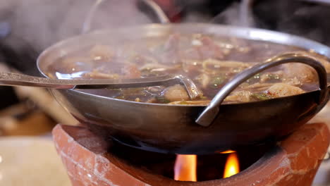 cooking and mixing a mixture of different meats in a piping hot thai noodle soup, a traditional food in thailand