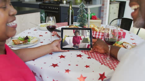 una pareja afroamericana sonriente usando una tableta para una videollamada de navidad con una mujer feliz en la pantalla