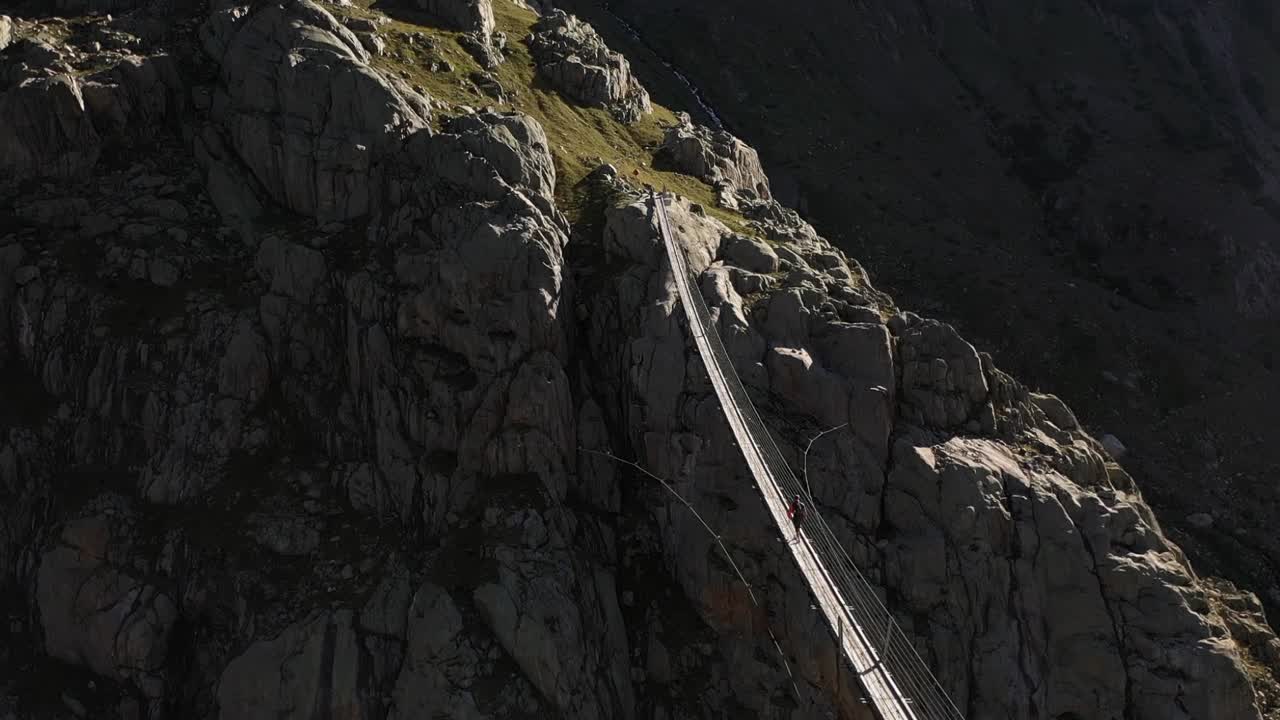 Una ripresa circolare di una persona che cammina da sola nel vasto paesaggio e nella natura selvaggia della Svizzera su un ponte sospeso durante un caldo pomeriggio di sole