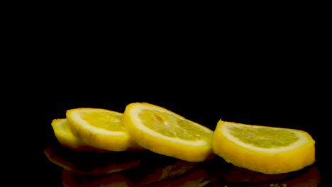 Yellow-lemon-falling-and-separating-into-slices-on-a-black-table