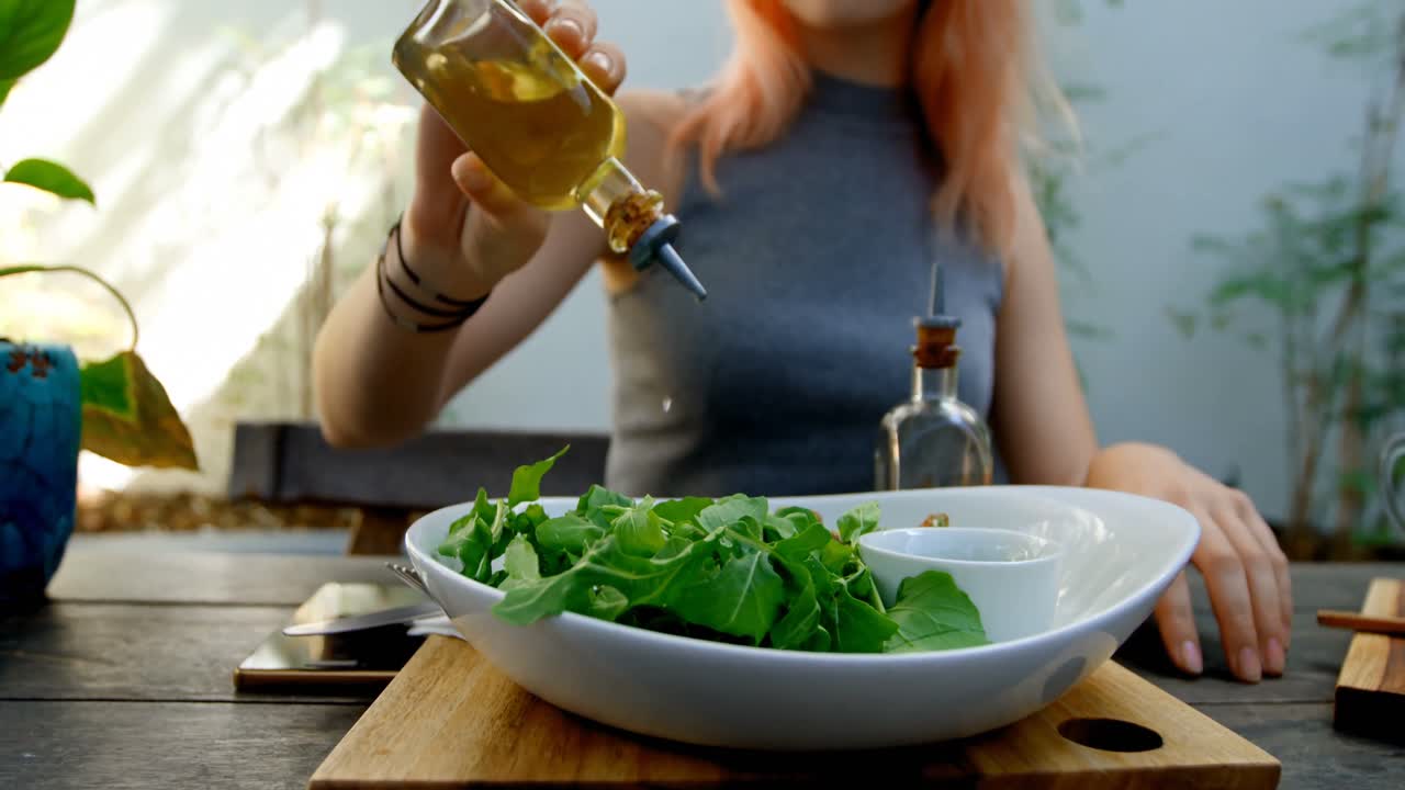 Mujer joven echando aceite de oliva en la ensalada 4k