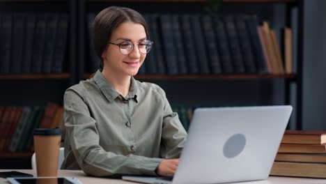 smiling confident woman business student in eyeglasses working chatting use laptop at library desk