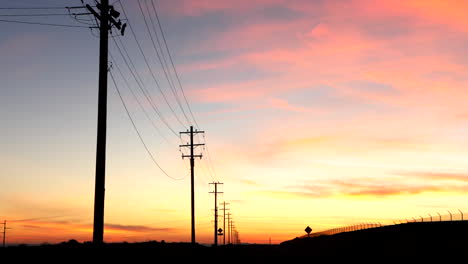 a colorful california sunrise sky looking down a road with telephone poles and electric wires in silhouette vanishing into the distance