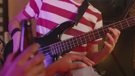 close up of an unrecognizable boy playing guitar while girl listening to him and drinking beer during a rehearsal in recording studio