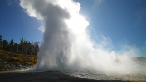 Filmischer-Großer-Alter-Treuer-Geysir,-Grelles-Sonnenlicht,-Sonnenaufgang,-Sonnenuntergang,-Eruption,-Explosion,-Dampf,-Yellowstone-Nationalpark,-Aussichtsplattform,-Oberes-Geysirbecken,-Herbst,-Schöner-Blauer-Himmel,-Zeitlupe,-Zoom