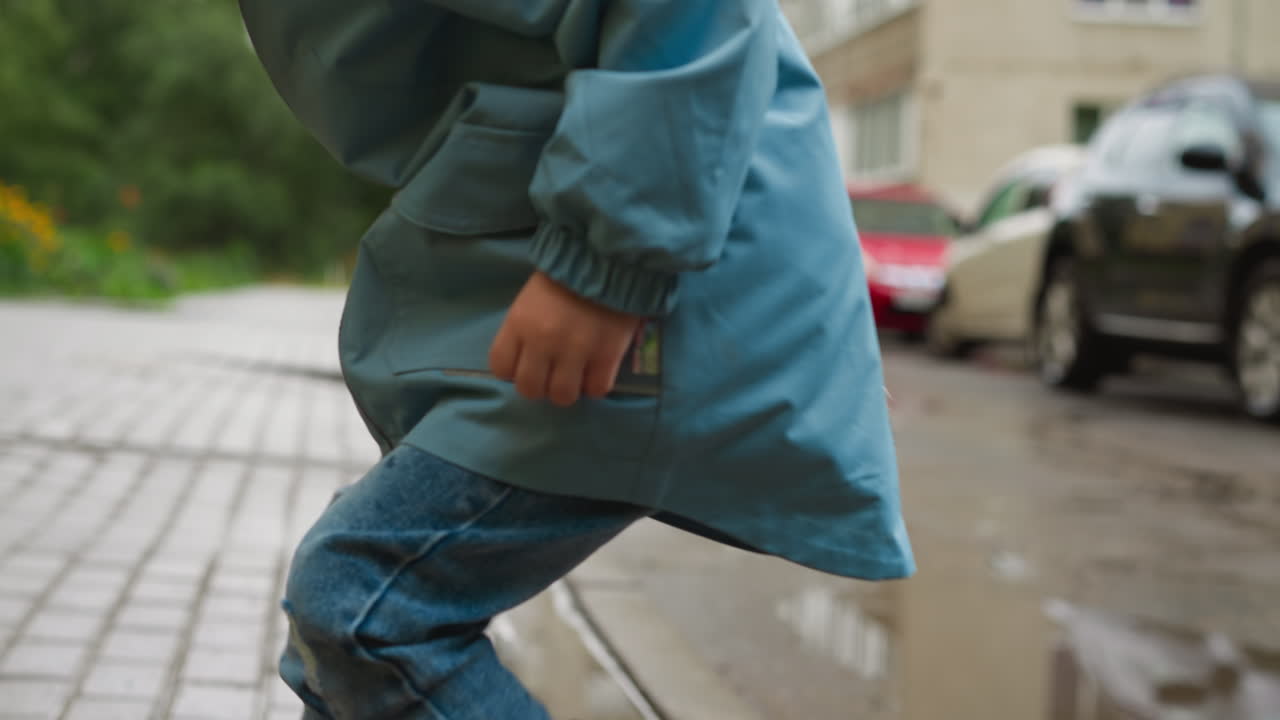 Child in rubber boots jumps on sidewalk kid playful spirit undampened by wet conditions near