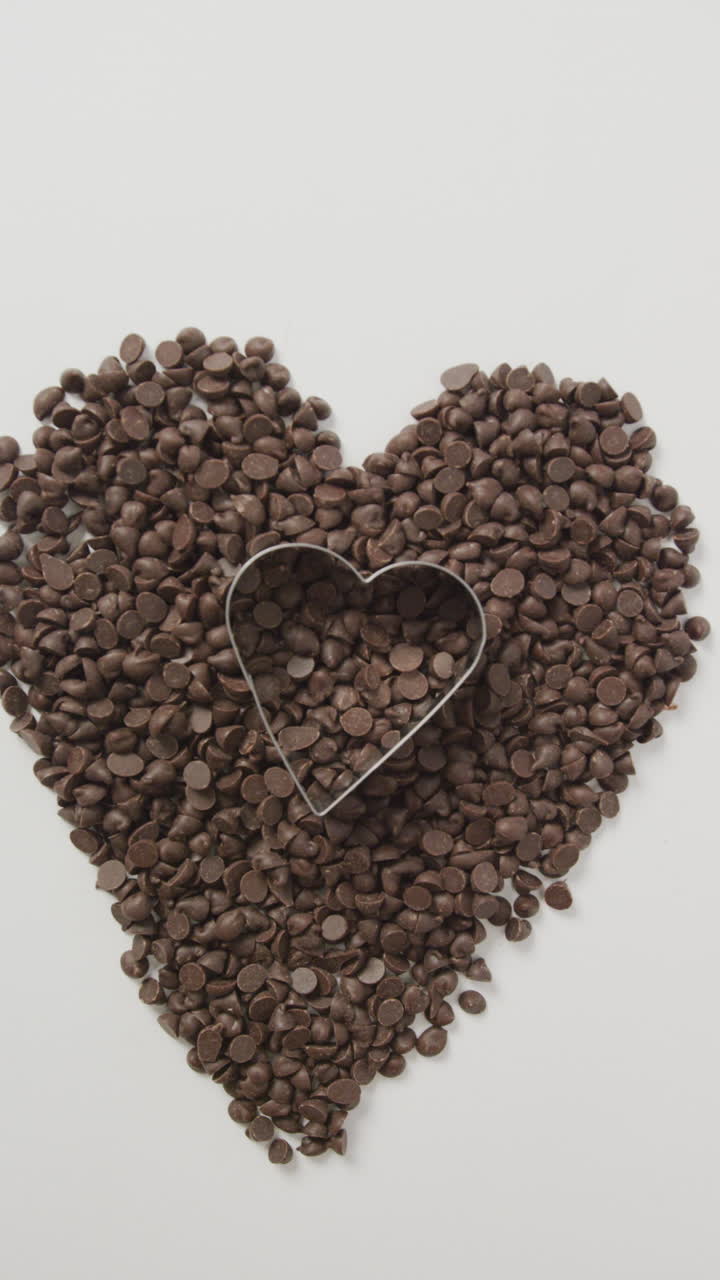 video vertical de trozos de chocolate formando un corazón con un cortador de galletas en forma de corazón sobre un fondo blanco