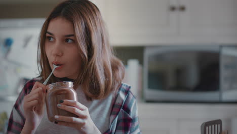 sneaky teenage girl eating chocolate spread from jar in kitchen enjoying delicious treat cheeky teen indulging in unhealthy snack at home