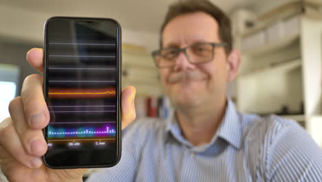 portrait shot of adult man showing process of stock market change on smartphone - digital animation on phone businessman with glasses in background