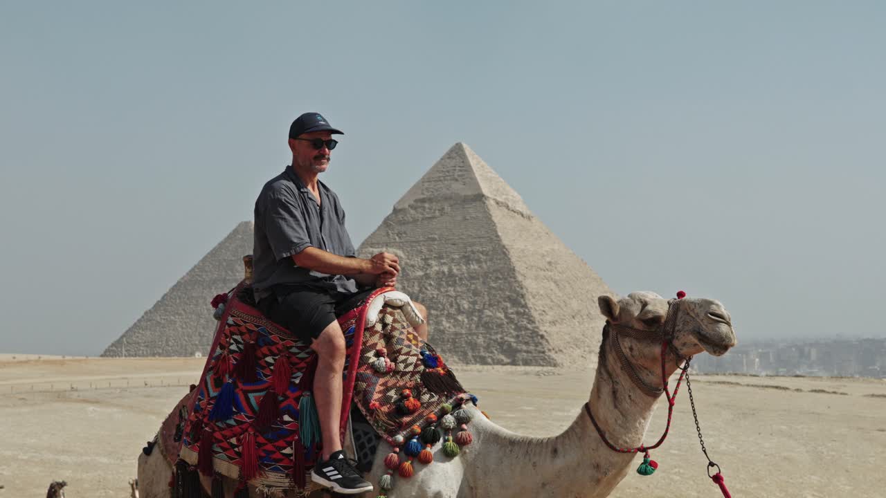 Esperienza di viaggio egiziana classica: un uomo seduto in cima a un cammello sull'altopiano di Giza. Il cammello è adornato con una sella vivace e dai motivi tradizionali.