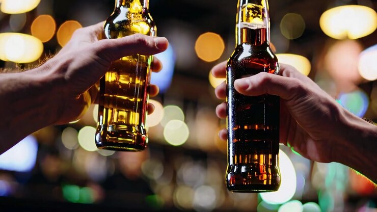 Primo piano di due mani che tengono bottiglie di birra in un bar vivace