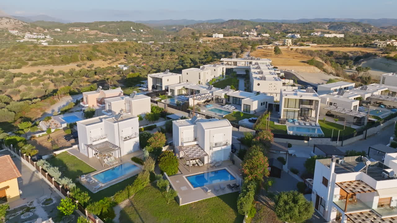 Aerial view circling modern vacation villas with pools, sunny morning in Greece