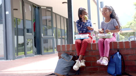 in school, two biracial young girls are enjoying lunch outside with copy space