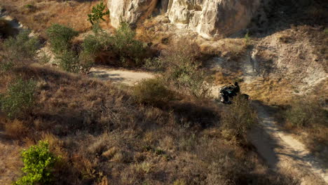 Woman-drives-quad-bike-through-Cappadocia-landscape,-Aerial-view