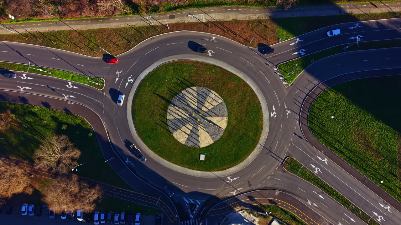 Rotatória com design geométrico vista de cima, mostrando veículos e caminhos durante o dia em uma área suburbana