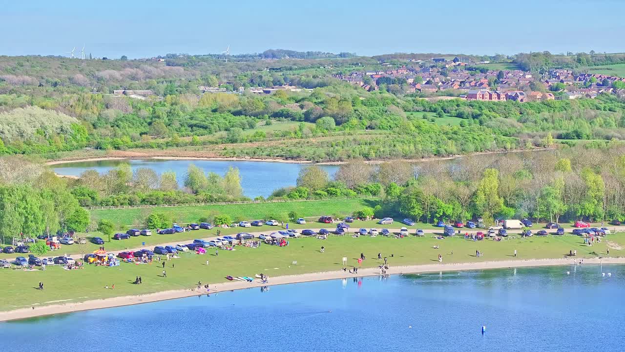 Aerial: people and cars next to the lake during the day in Rother Valley Country Park in the Metropolitan Borough of Rotherham, South Yorkshire, England, crane up drone shot