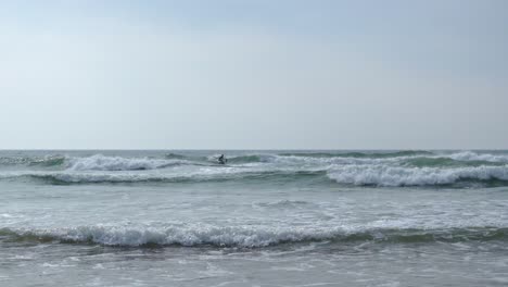 Sit-down-paddle-boarder-in-the-water-off-Mawgan-Porth-beach,-Cornwall,-UK
