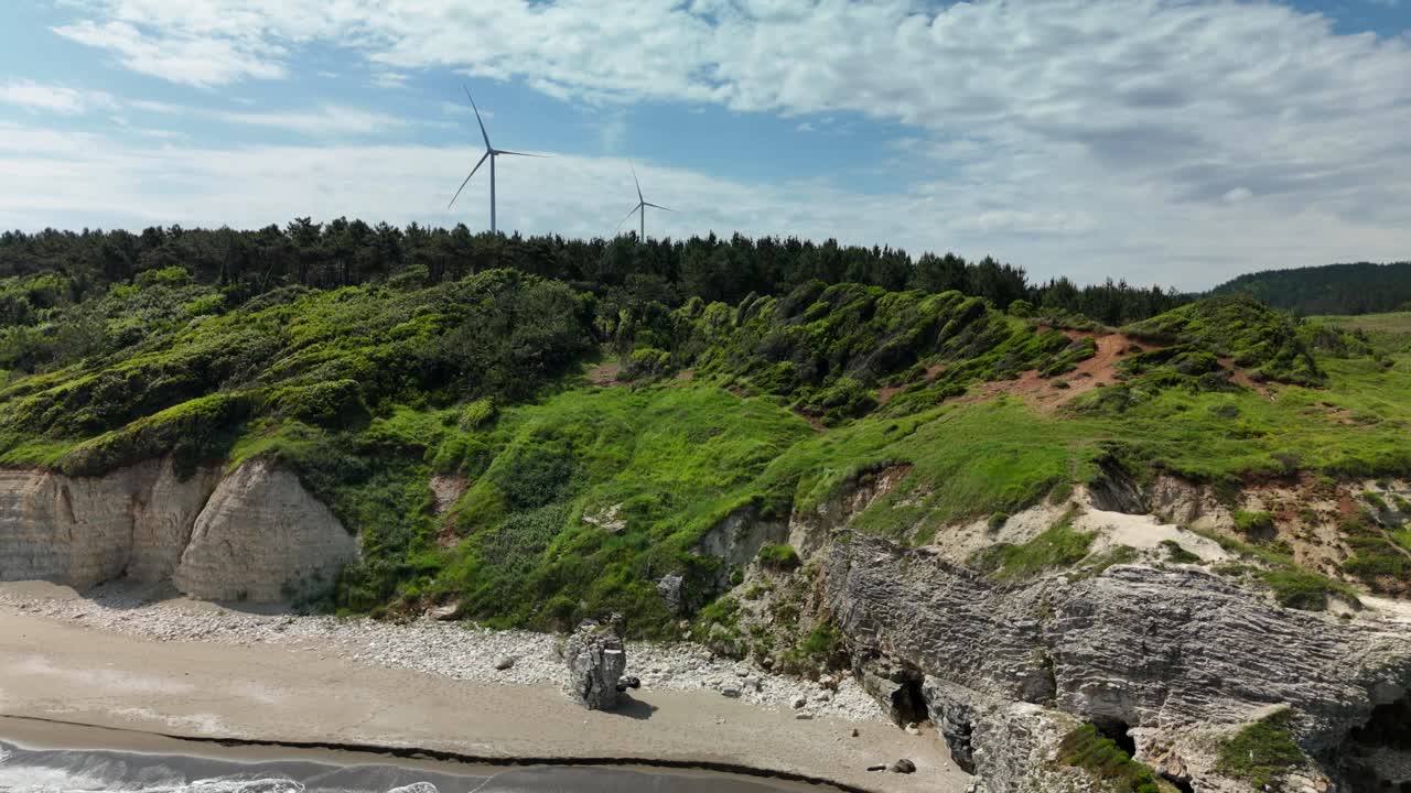 Lush green cliffs with wind turbines under a cloudy sky, serene atmosphere