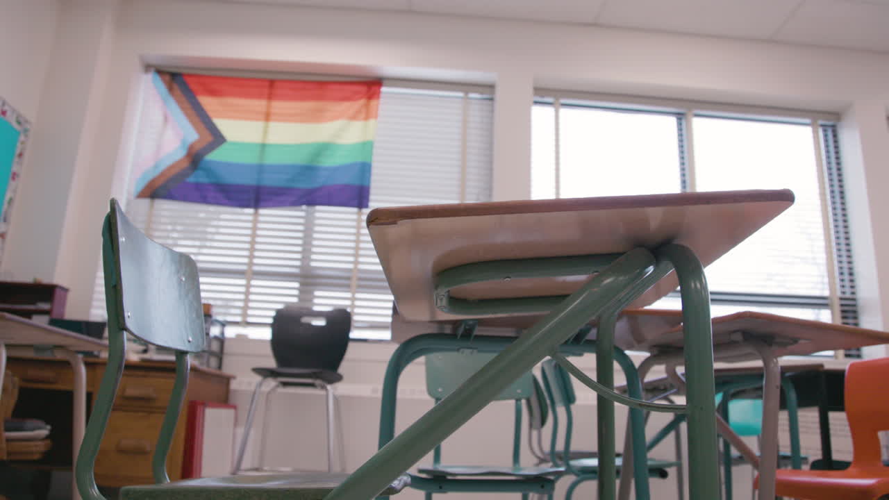Una scrivania in un'aula con una bandiera pride sul muro di un ambiente scolastico