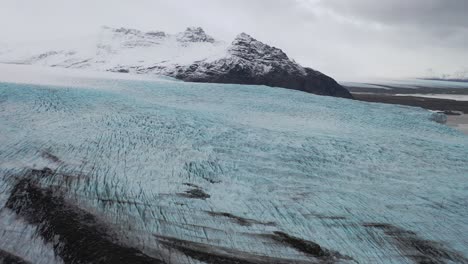 Aerial-of-a-glacier-frozen-by-a-snowcovered-mountain-range-in-Iceland