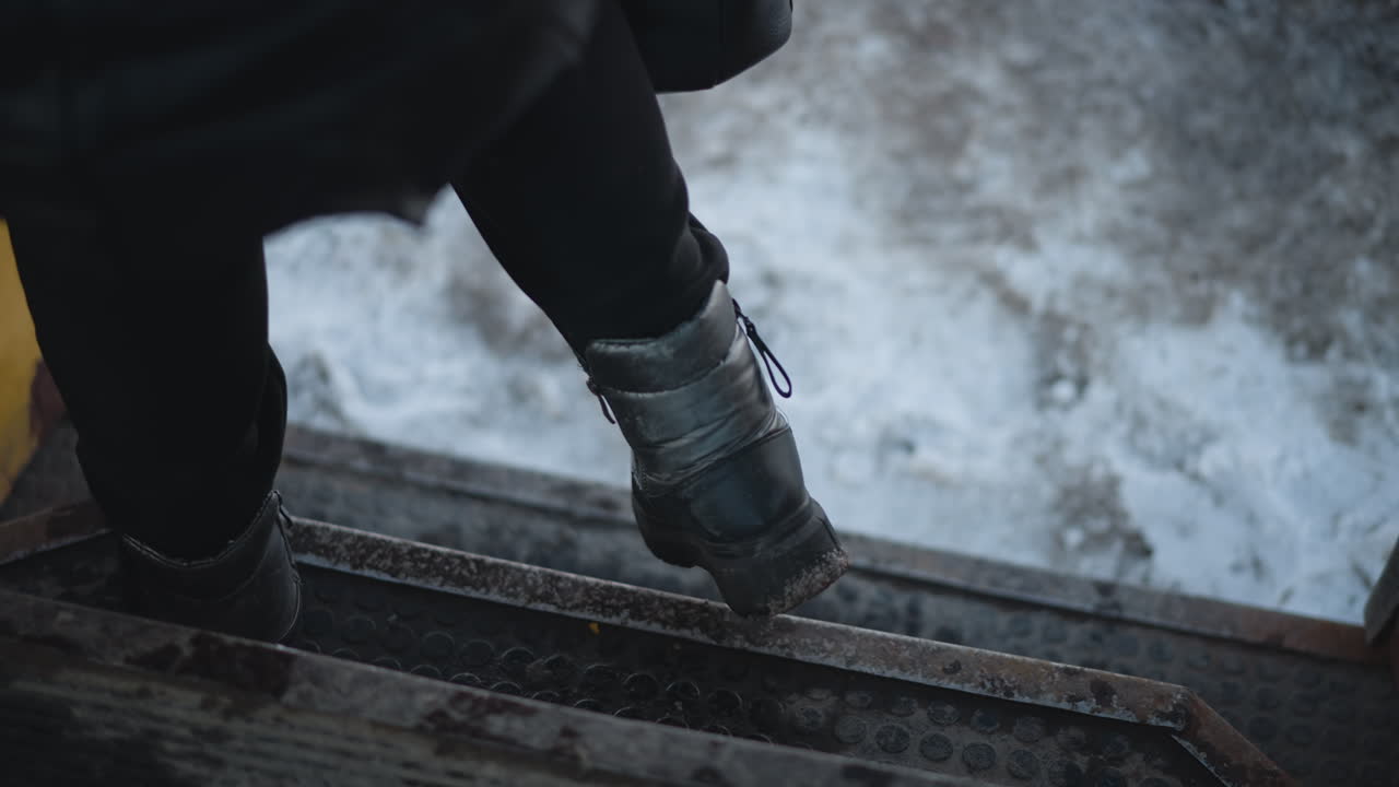 Low interior view of locked yellow train door over snowy ground, hinges, door begins opening as passenger steps out at stop, and rubber tread shake with motion during cold winter ride inside
