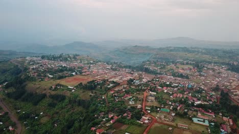 drone captures expansive view of kapchorwa town nestled on mount elgon’s lush slopes, with scattered homes, red roads, and distant hills fading into mist under a calm late afternoon light