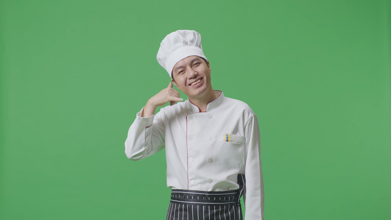 Asian Man Chef Smiling And Making Call Me Gesture To Camera While Standing In The Green Screen Background Studio