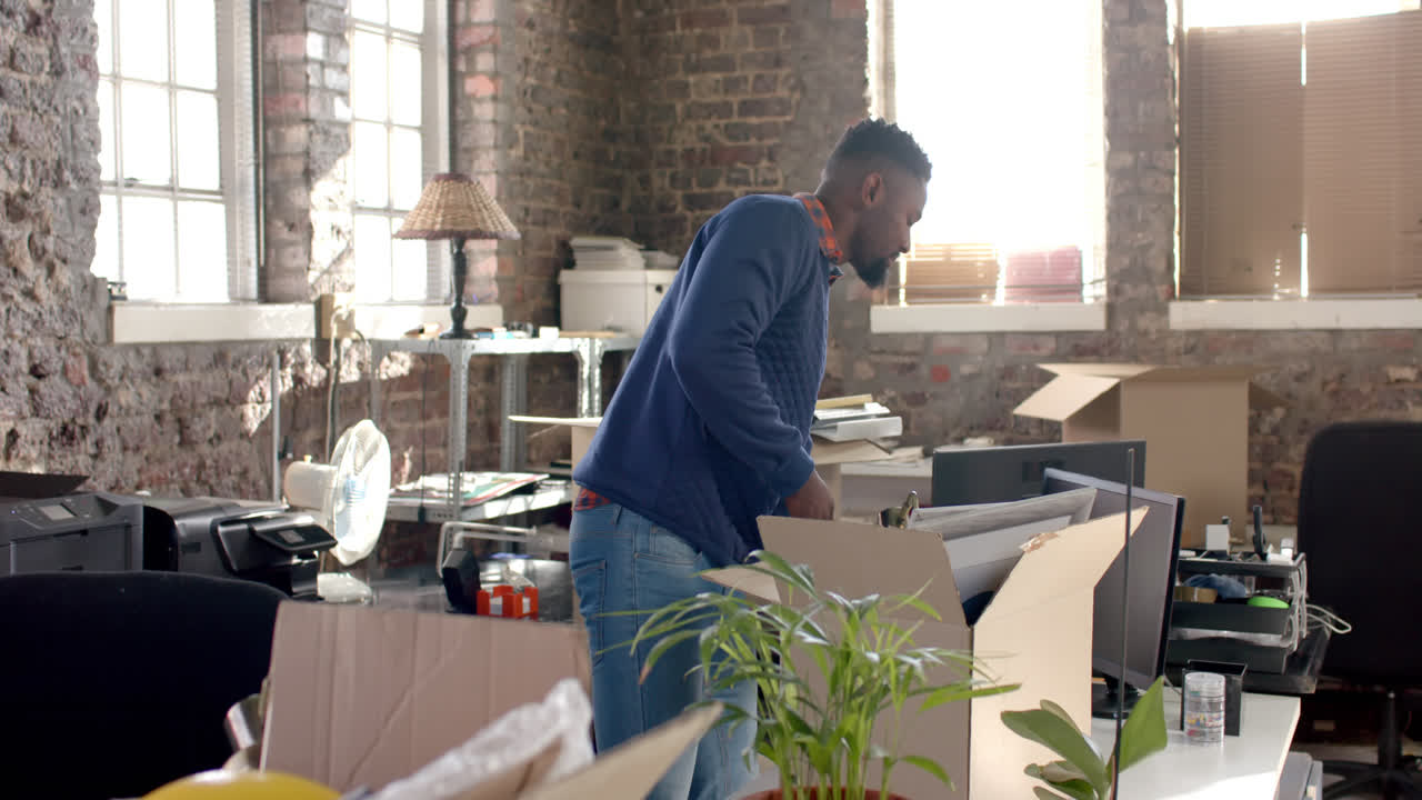 Happy african american casual businessman holding box with documents in office in slow motion