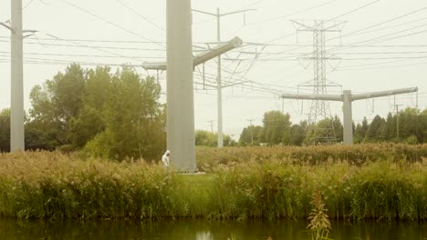 Man-inspecting-field-with-large-electrical-lines-in-Hazmat-suit