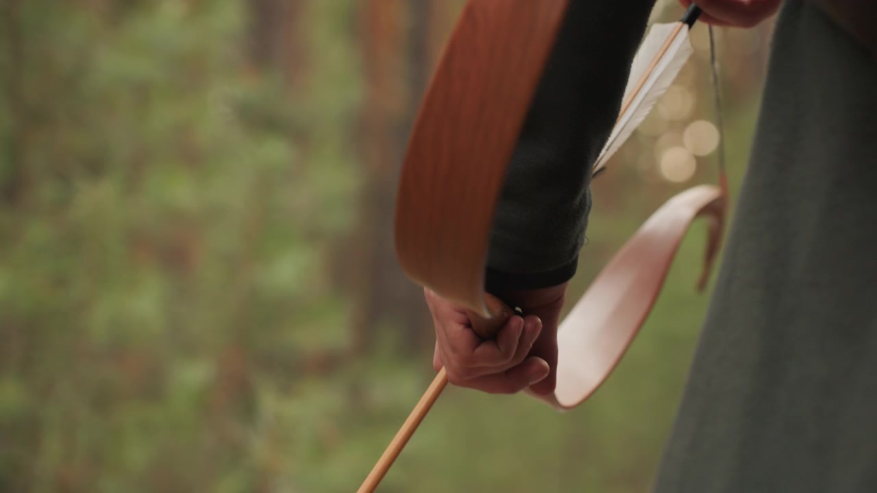 Vue rapprochée d'un archer en forêt, tenant un arc en bois et tendant la corde sur une flèche encoched, montrant une forte tension, une visée stable et un mouvement prêt sous une douce lumière naturelle, avec l'archer, l'arc.