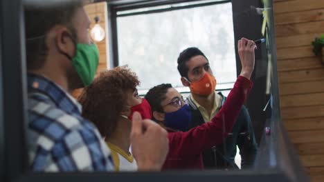 diversos colegas con máscaras de cara escribiendo en tablero de vidrio discutiendo juntos en una oficina moderna
