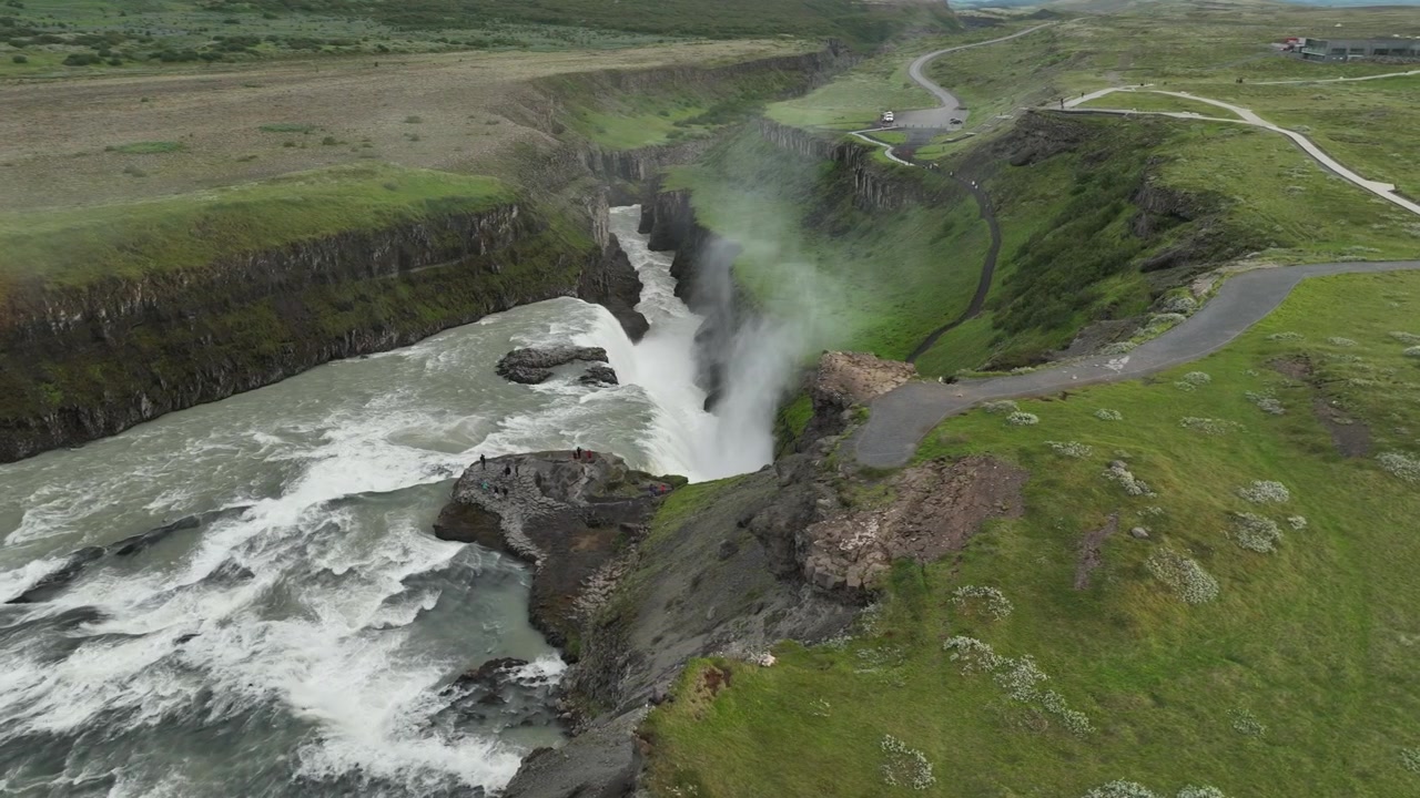 Une vue aérienne panoramique de la cascade de Gullfoss en Islande, mettant en valeur la rivière puissante, les falaises rocheuses et les plaines verdoyantes environnantes