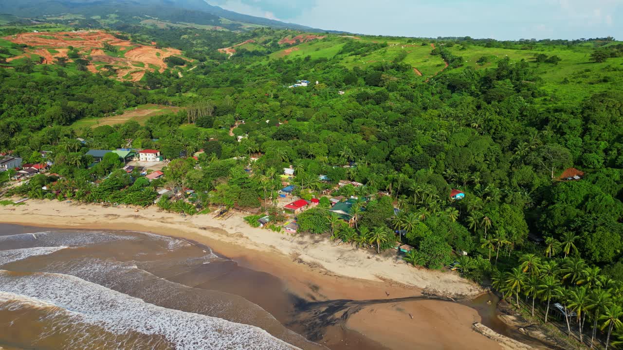 Tilt‑down aerial revealing black sand patterns along the shoreline as waves crash onto the coast, framed by lush tropical scenery at Quinawan Beach in Mariveles, Bataan, Philippines