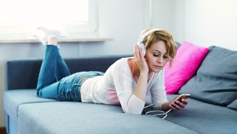 woman is lying on the couch and listening to music
