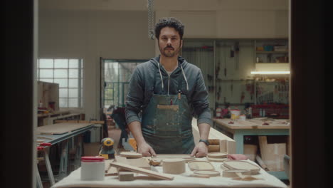 portrait of woodworker in stained apron at workplace in woodshop