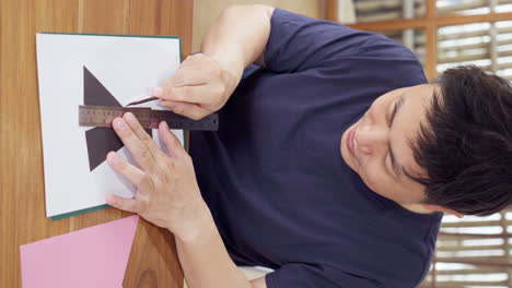 asian man doing diy craft project by cutting paper using utility knife cutter with ruler on cutting mat