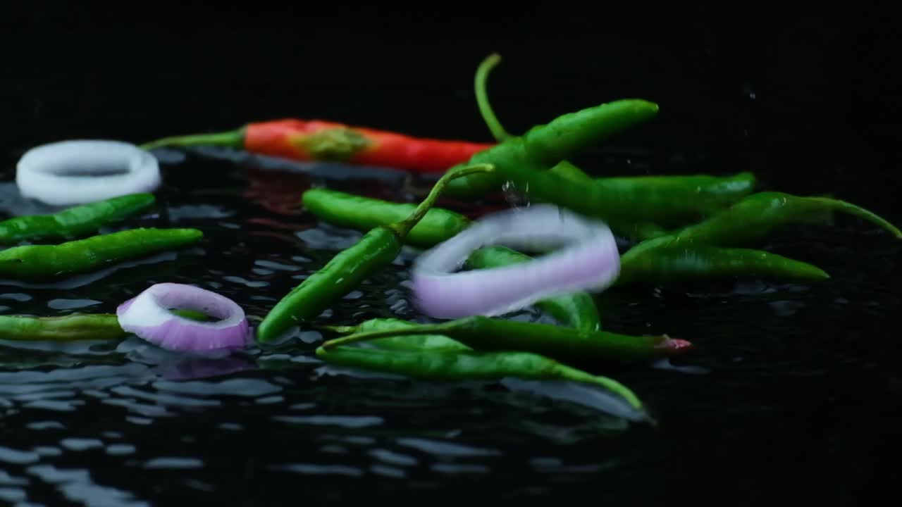 Chili and onion rings falling on wet black surface, studio shot