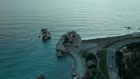 Vista-Aérea:-Vista-Al-Atardecer-De-La-Formación-Rocosa-Cerca-De-La-Costa-Y-La-Carretera-Sinuosa