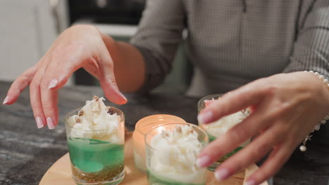 pastry chef delicately rotates cups of beautifully decorated ice cream with both hands on wooden table beside glowing candle in cozy kitchen creating warm inviting atmosphere of creativity and joy