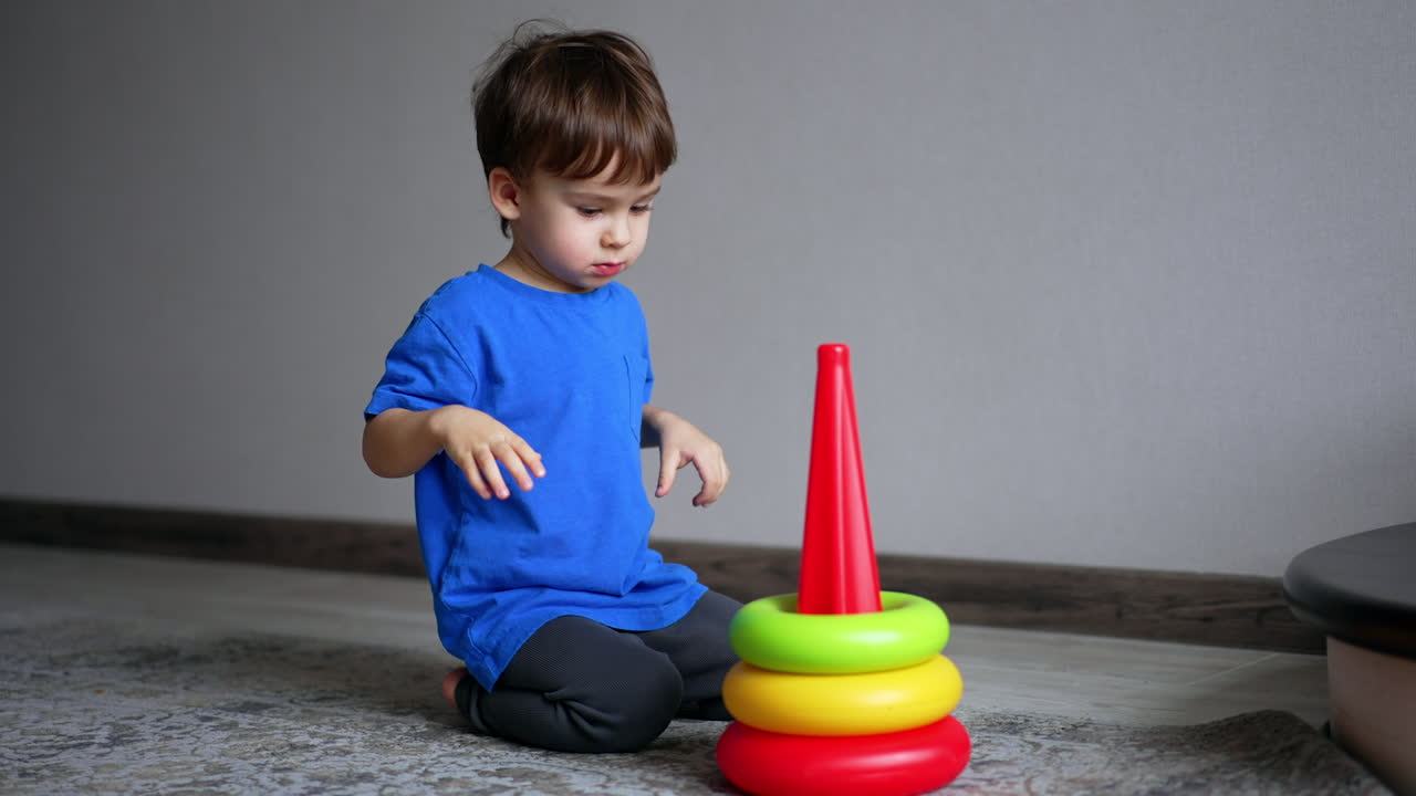Energetic Caucasian boy plays with toy pyramid. Play time for a toddler at home.